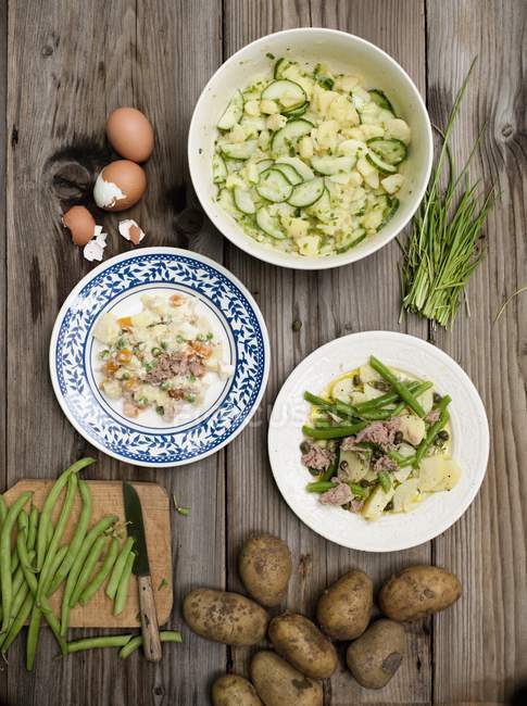 Drei verschiedene Kartoffelsalate auf hölzerner Oberfläche — Stockfoto