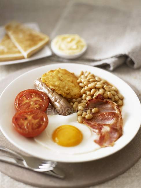 Английский завтрак с яичницей, беконом и фасолью на белой тарелке — стоковое фото