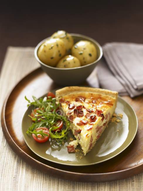 A slice of quiche lorraine with rocket salad and a side dish of potatoes on plate — Stock Photo
