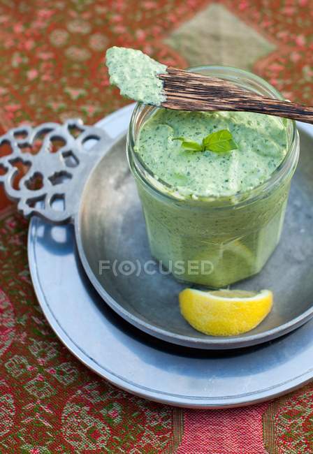 Vista sopraelevata di un barattolo aperto di salsa alle erbe con coltello in legno e spicchio di limone — Foto stock