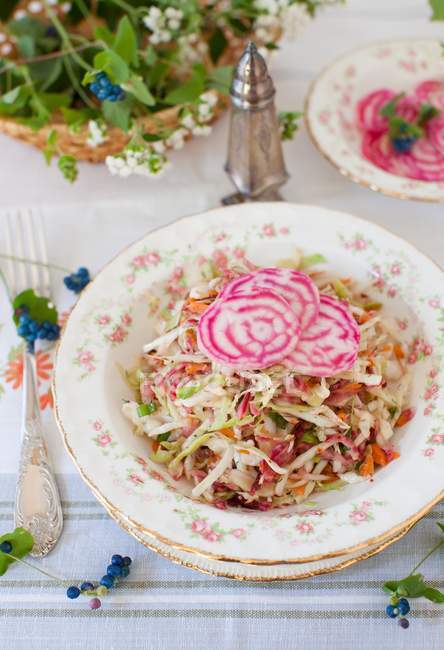 Salada de repolho coberta com beterrabas variegadas fatiadas; Em uma mesa com uma cesta de flores — Fotografia de Stock