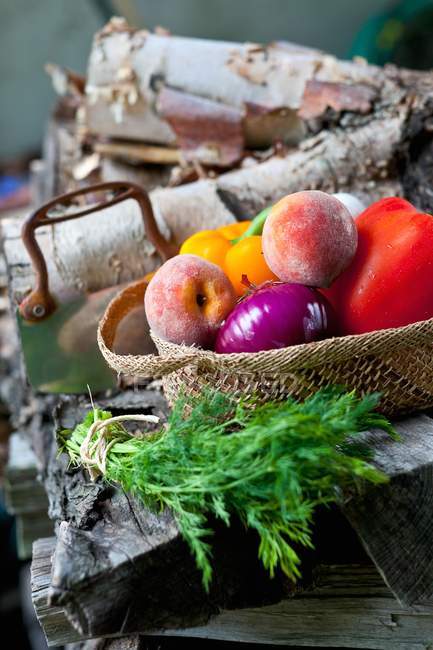 Légumes et fruits frais dans un panier ; bouquet de plume fraîche sur une pile de bois — Photo de stock
