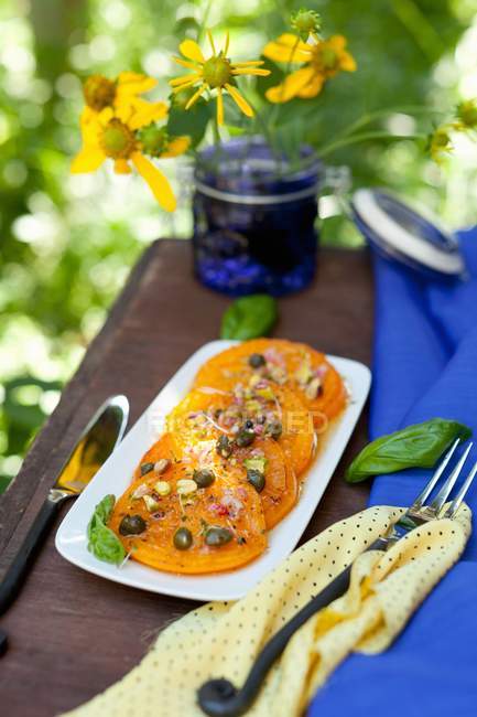 Pfanne gebratene gelbe Tomaten mit Pistazienkapern; auf einem Teller auf einem Tisch im Freien — Stockfoto