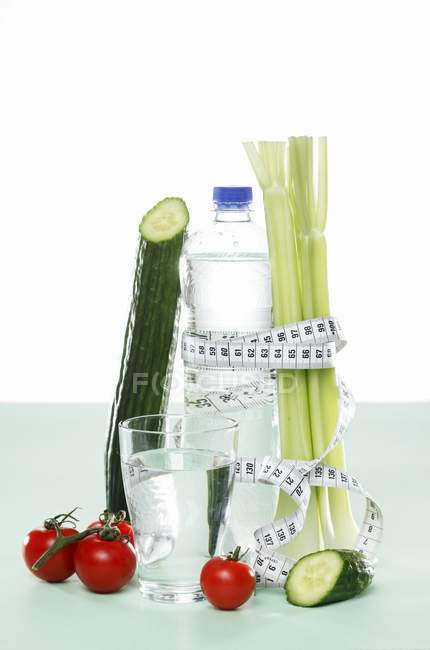 Verduras y agua con cinta métrica sobre fondo blanco - foto de stock