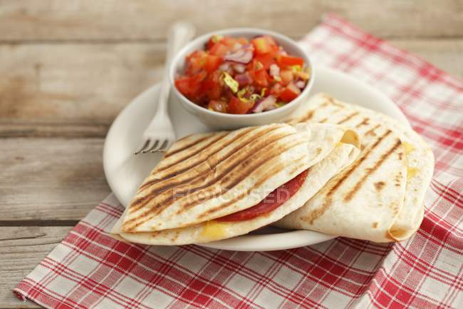 Quesadillas with salami and tomato salsa on plate with saucer over table — Stock Photo