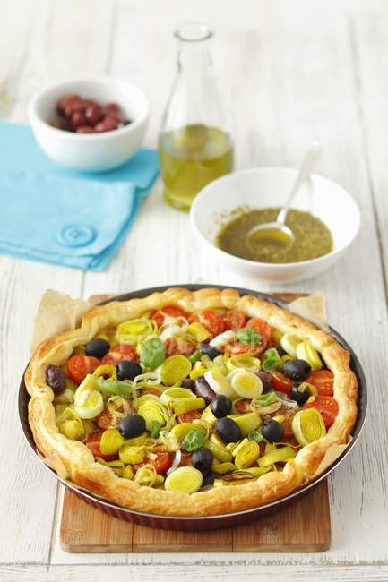 Пафосный пирог с помидорами, луком-порей, оливками и базиликовым песто на деревянной поверхности — стоковое фото