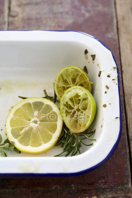 Vue rapprochée des tranches de citron, des citrons verts pressés et du romarin dans une boîte à rôtir — Photo de stock
