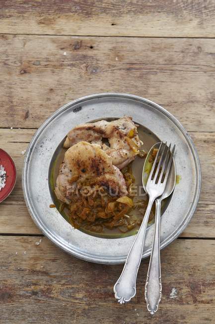Chicken with pomegranate sauce on plate with fork and knife over wooden surface — Stock Photo