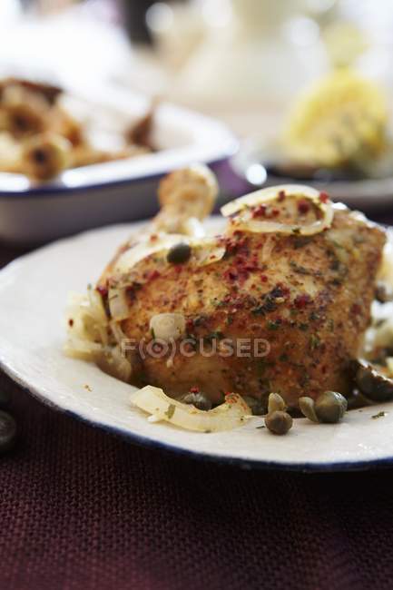 Куриная нога с оливками и каперсами на белой тарелке — стоковое фото