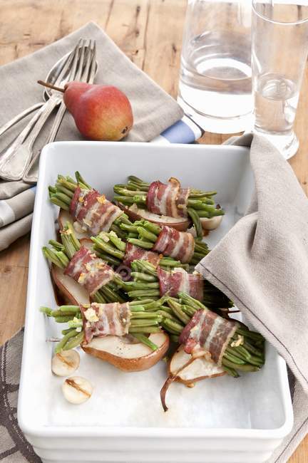 Roasted beans wrapped in bacon on top of baked pears in dish — Stock Photo