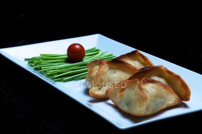 Sambusak pastry parcels with vegetables on white dish and black background — Stock Photo