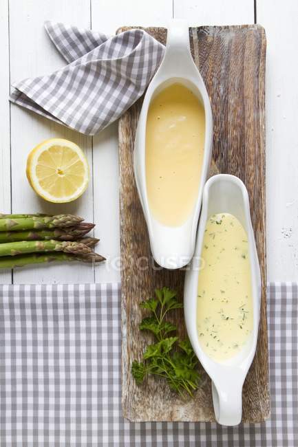 Two sauces served with asparagus on wooden desk — Stock Photo