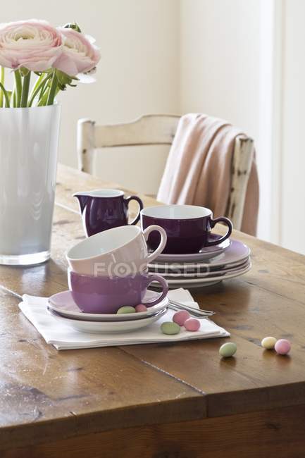 Placas empilhadas e xícaras de café perto de flores Ranunculus rosa em um vaso — Fotografia de Stock