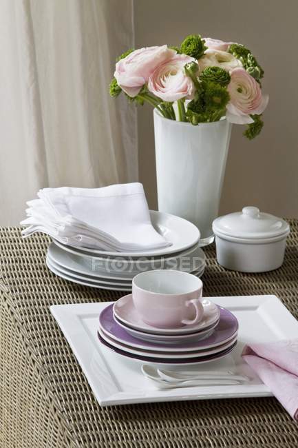 Vue surélevée des assiettes empilées et des tasses à café avec un bouquet de fleurs de ranunculus roses — Photo de stock