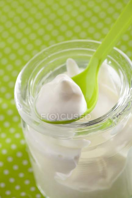 Vista de cerca de la crema agria en un frasco y en una cuchara verde - foto de stock
