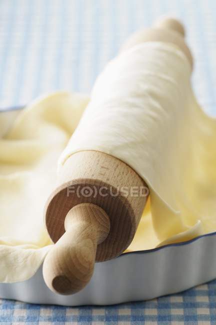 Vue rapprochée de la pâte roulée sur un rouleau à pâtisserie et dans un plat à tarte — Photo de stock