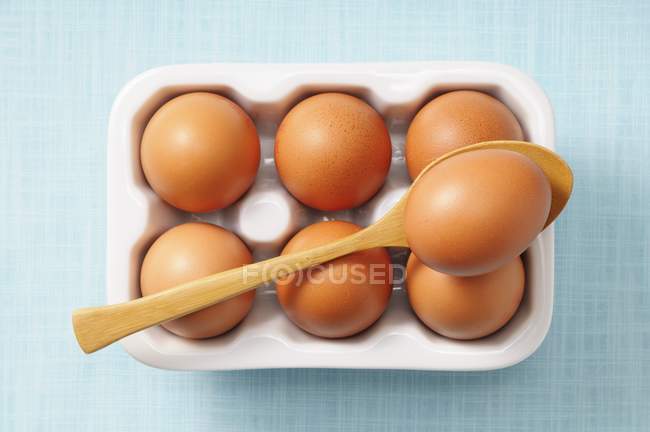 Бурые яйца в коробке с деревянной ложкой — стоковое фото
