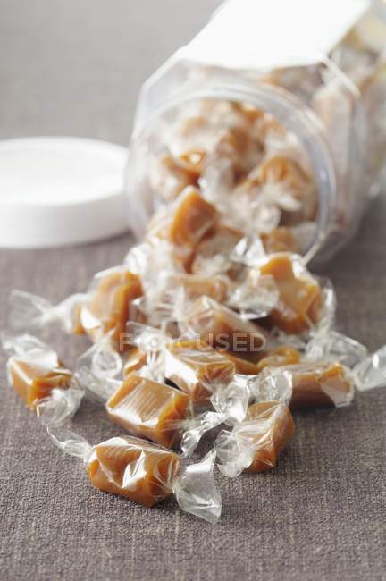 Closeup view of wrapped toffees and overturned storage jar — Stock Photo