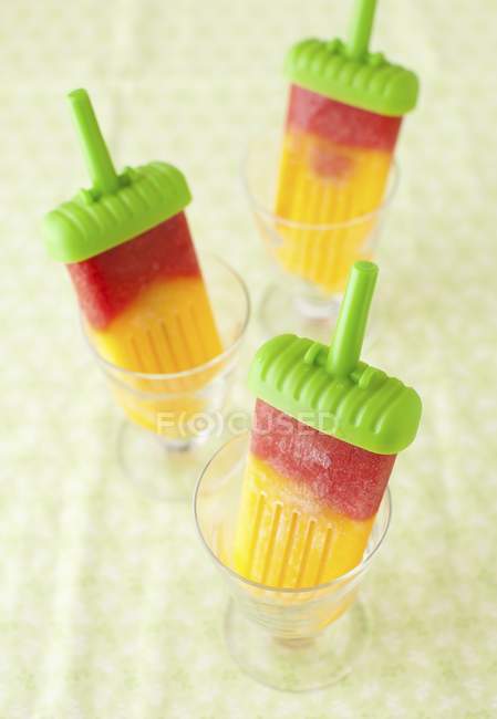 Vue rapprochée des popsicles à la mangue et à la fraise dans des tasses en verre — Photo de stock