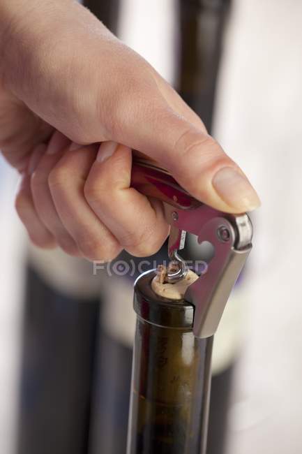 Vista de cerca de la botella de apertura de la mano de vino con sacacorchos - foto de stock