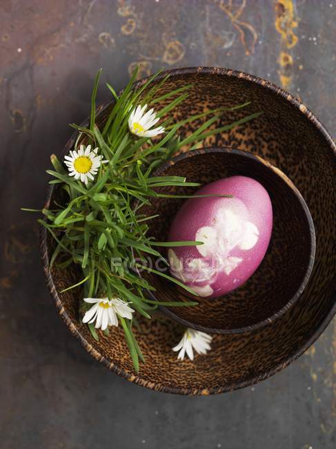 Vista superior de un huevo rosa decorado para Pascua en un tazón de madera con margaritas - foto de stock