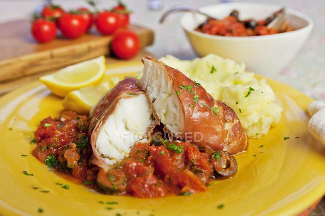 Cod wrapped in prosciutto with tomato sauce — Stock Photo