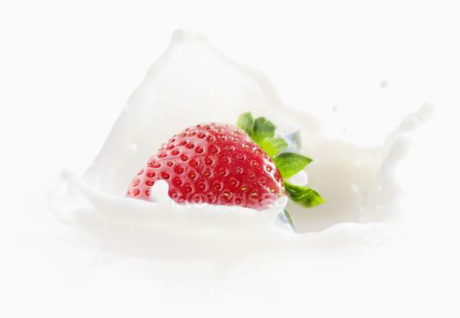 Strawberry falls into milk — Stock Photo