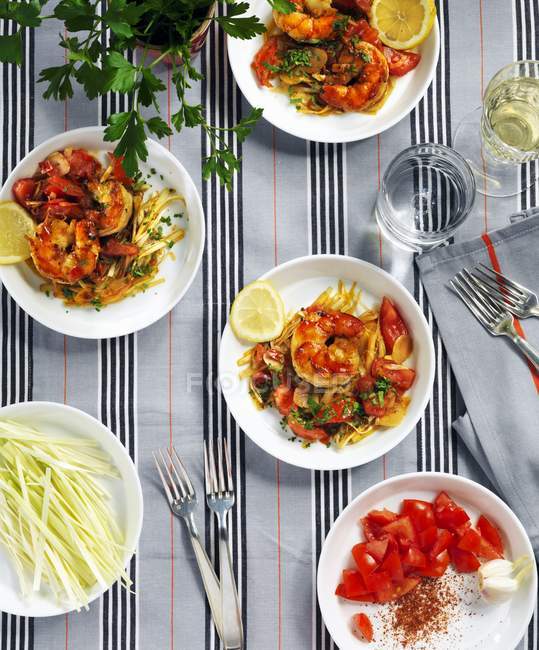 Креветки с томатным салатом на белых тарелках на скатерти — стоковое фото