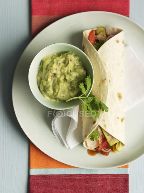 Fajitas filled with vegetables and served with guacamole in white plate over towel — Stock Photo