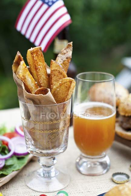 Kartoffelkeile auf einem Tisch draußen, im Hintergrund Büffelburger und eine US-Fahne — Stockfoto