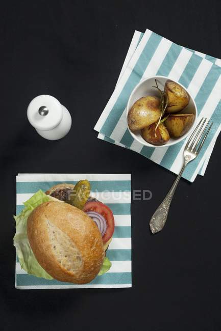 Una hamburguesa con lechuga, tomate y pepinillo, servida con patatas de romero - foto de stock
