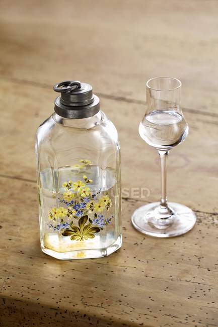 Nahaufnahme einer alten Flasche mit bemalten Blumen und einem Glas Schnaps — Stockfoto