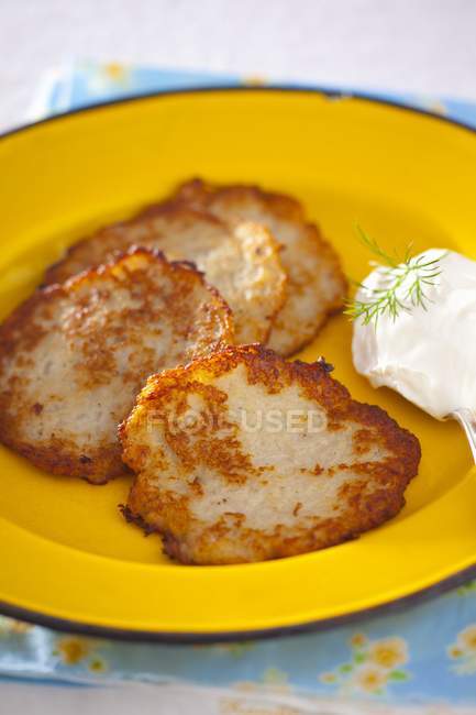 Potato fritters with a blob of sour cream on orange plate — Stock Photo