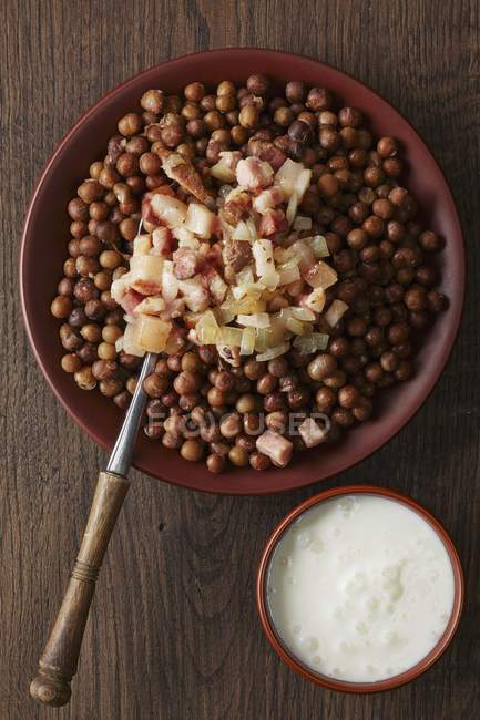 Grey peas with bacon and onions over wooden surface — Stock Photo