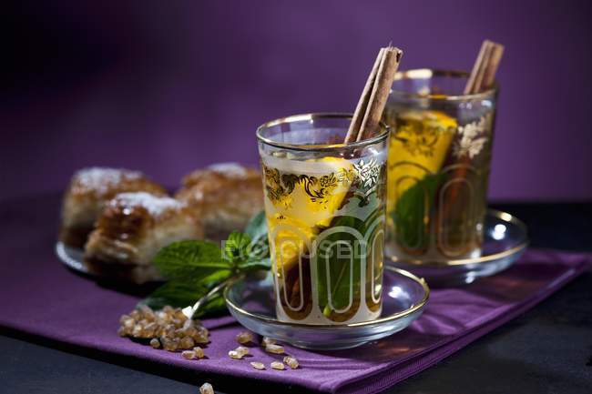Tea Eastern-style with mint, cinnamon, orange and baklava over purple surface — Stock Photo