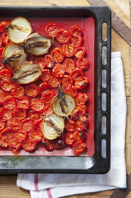 Жареные помидоры черри и лук в подносе для выпечки на деревянной поверхности — стоковое фото