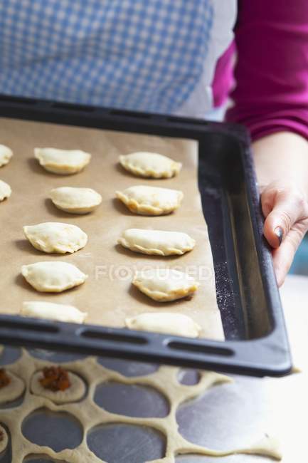Closeup view of a woman holding a baking tray of raw pastry parcels — Stock Photo