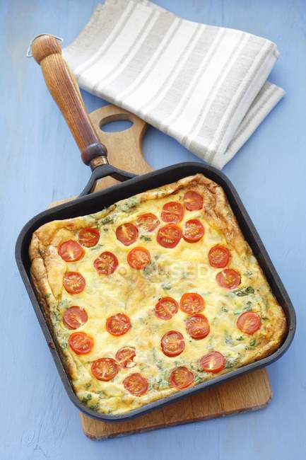 Potato tortilla with cherry tomatoes in baking tray over wooden desk — Stock Photo