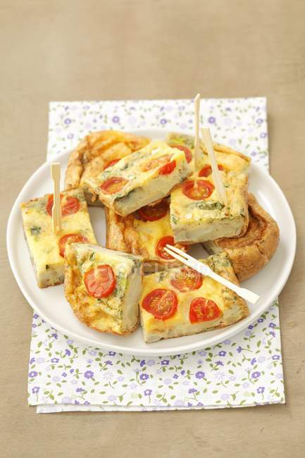 Potato tortilla with cherry tomatoes on white plate over towel — Stock Photo