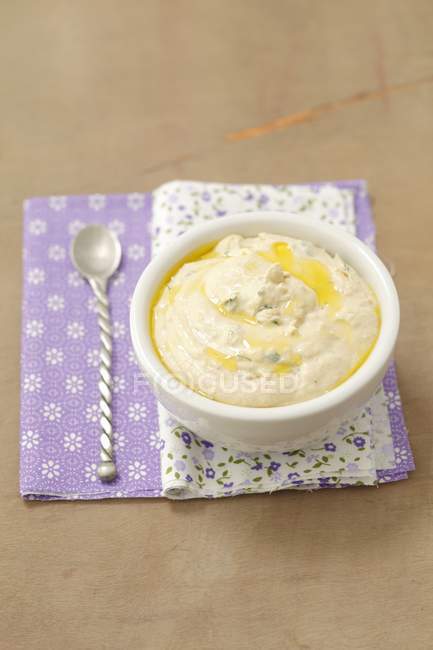 Hummus y aceite en un tazón blanco con una cuchara en una servilleta plegada con dibujos florales - foto de stock