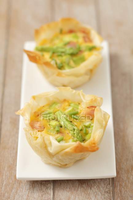 Mini Filo pastry quiches with asparagus over wooden surface — Stock Photo