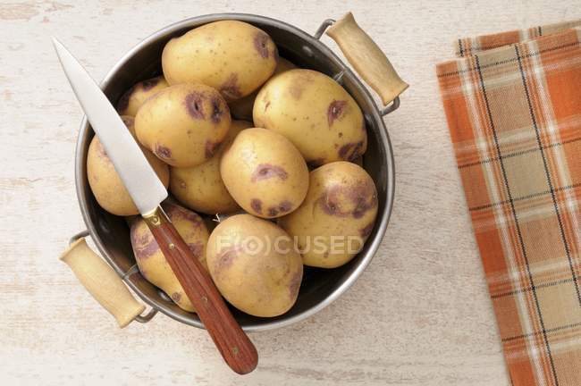 Fresh Potatoes in colander with knife — Stock Photo