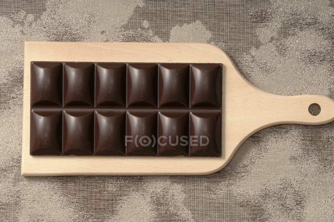 Bar of dark chocolate on chopping board — Stock Photo