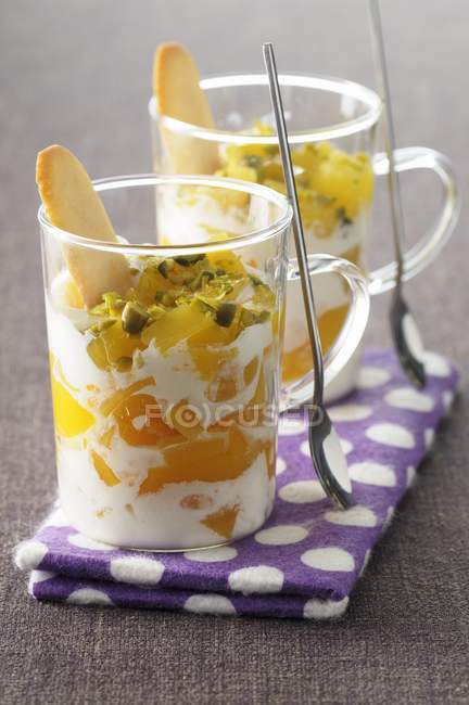Trifle pêssego com pistache em óculos com colher sobre toalha — Fotografia de Stock