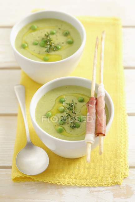 Sopa de guisantes verdes con grissini en cuencos sobre toalla amarilla con cuchara - foto de stock
