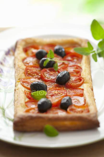 Пафосный пирог с помидорами черри, оливками и ореганом на белой тарелке — стоковое фото