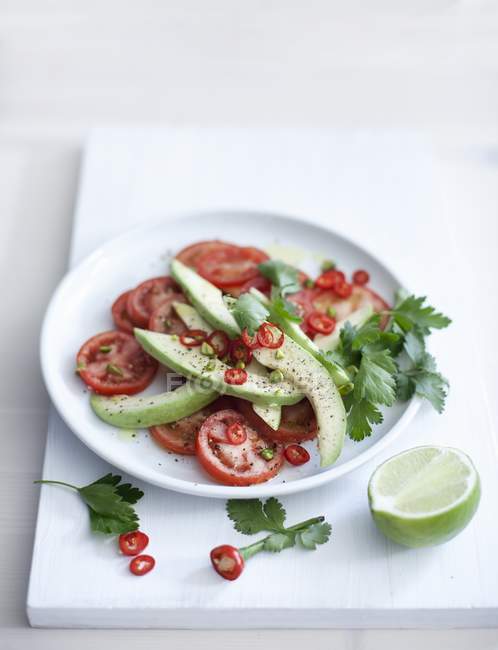 Salada de tomate-abacate com anéis de pimenta na placa branca sobre mesa — Fotografia de Stock