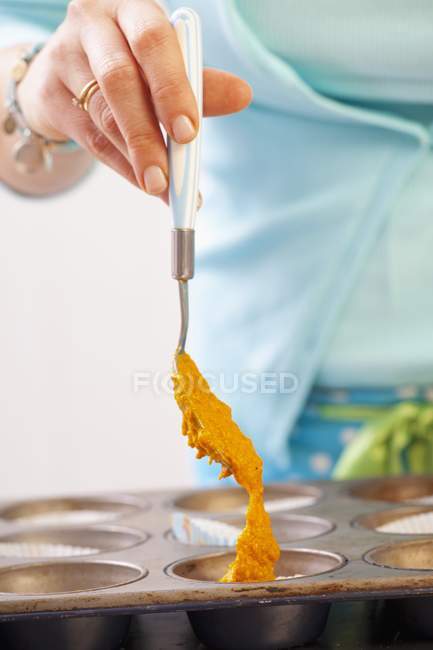 A woman spooning carrot cake batter into a baking tin, midsction — Stock Photo