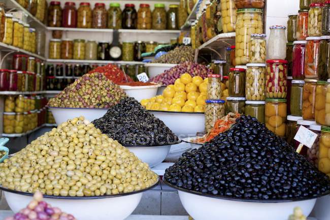Viele Gläser mit verschiedenen Konserven und Berge von Oliven in einem Geschäft — Stockfoto