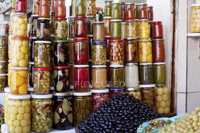 Lotes de frascos de alimentos conservados variados e montes de azeitonas em uma loja — Fotografia de Stock